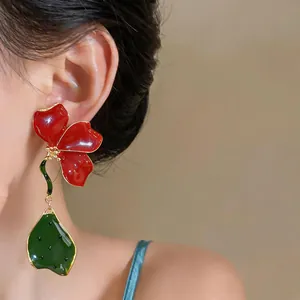 Détail d'une grande boucle d'oreille fleur en émail rouge avec goutte feuille verte
