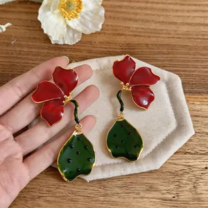 Détails des boucles d'oreilles fleurs en émail rouge et feuilles vertes sur tissu