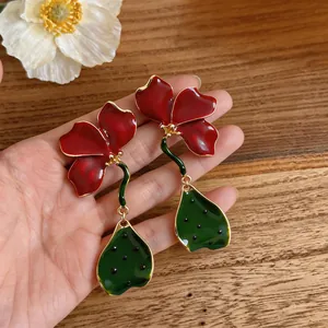 Détail macro de boucles d'oreilles fleurs en émail rouge avec pétales en métal doré et feuilles