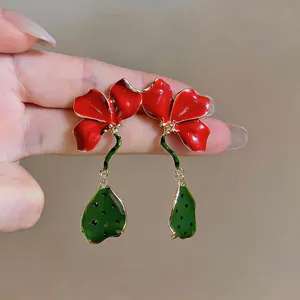 Vue détaillée des boucles d'oreilles fleurs rouges émaillées avec feuilles vertes.