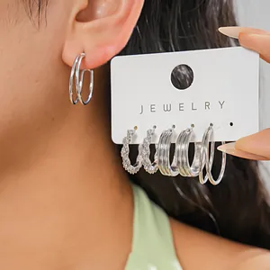 Detailed macro view of 6-piece silver geometric hoop earrings set on display card and model's ear