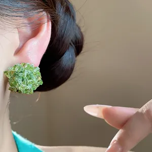 Vista macro de pendientes de botón de flor de cristal verde con agujas de plata en oreja