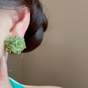 Primer plano de un pendiente de flor con cuentas de vidrio verde con agujas de plata
