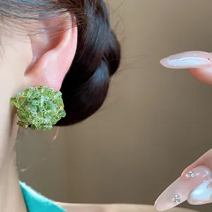 Primer plano de elegantes pendientes de botón con flores de cristal verde en la oreja