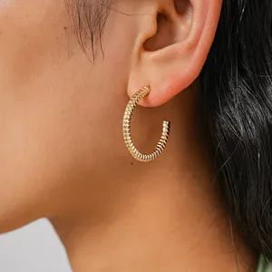 Macro view of gold twisted hoop earrings with an elegant spiral texture worn on the ear.