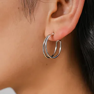 Close-up of minimalist silver metallic double hoop earrings worn on ear for elegant look