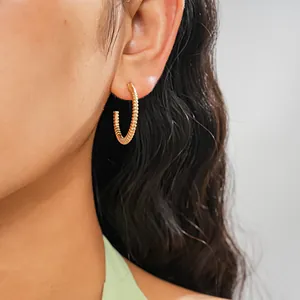 Close-up detail of a textured gold-colored geometric hoop earring for women.