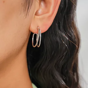 Close-up view of minimalist silver geometric rectangular hoop earrings worn on an ear model