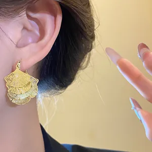 Nahaufnahme eleganter fächerförmiger Ginkgoblatt-Ohrringe aus Gold am Ohr