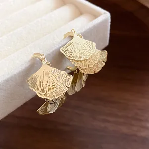 Detailansicht von goldenen Ginkgoblatt-Ohrringen an einer beigen Samt-Schmuckschatulle.
