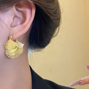 Detailaufnahme von geschichteten goldenen Ginkgoblatt-Ohrringen in Fächerform am Ohr