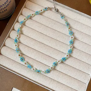 Détail en gros plan montrant les motifs de fleurs en perles bleues et blanches du collier.