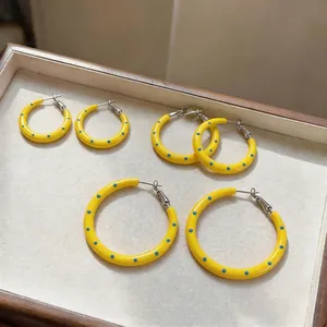 Orecchini a cerchio in smalto giallo a pois blu in tre misure, presentati in un vassoio.