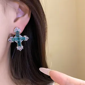 Close-up of a teal zircon cross stud earring worn on an ear for a luxury detail look