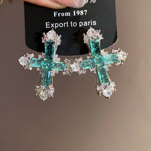 Detail showing elegant cross earrings with emerald green zircons and white crystals.