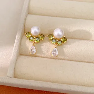 Primo piano elegante di orecchini placcati oro con perla bianca e zirconi verdi pendenti.
