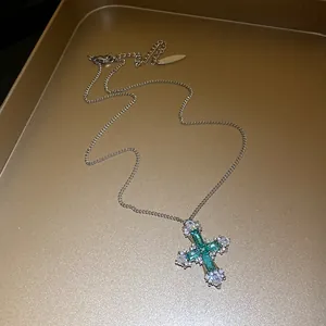 Detailed view of an elegant silver cross pendant necklace with green and clear zircon stones.