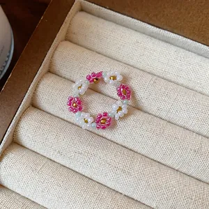 Gros plan d'une bague artisanale en perles de verre aux motifs floraux roses et blancs délicats