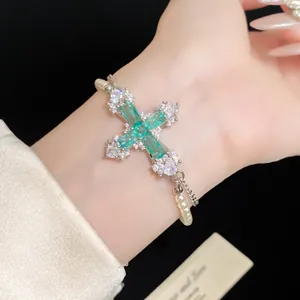Close-up of elegant emerald green zircon cross bracelet on woman's wrist with pearls.