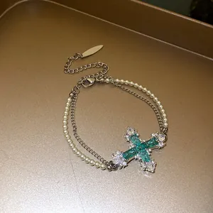 Detail view of a double-layered pearl and chain bracelet with a blue zircon cross.