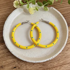 Dettaglio ravvicinato di orecchini a cerchio giallo vibrante con pois blu giocosi