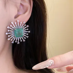 Close-up view of a luxury sunburst stud earring featuring a square green center stone