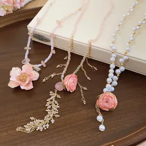 Dettaglio di tre collane con pendenti di rose rosa stabilizzate, perle e cristalli