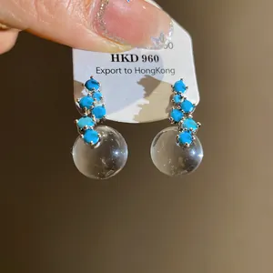Detailed view of silver stud earrings with blue stones and clear resin sphere pendants