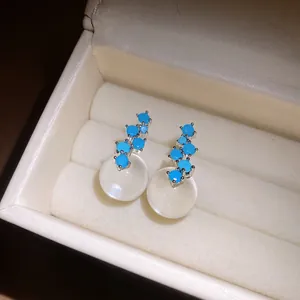Close-up detail of silver stud earrings with blue stones and resin spheres in a box