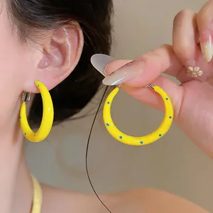 Dettaglio di orecchini a cerchio in smalto giallo con pois blu indossati da una modella