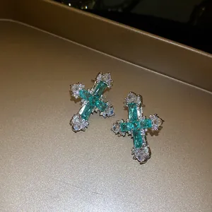 Close-up of cross stud earrings with emerald green and white zirconia stones.