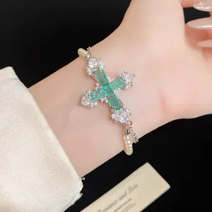 Detailed macro view of an emerald green and white zircon cross bracelet on wrist.