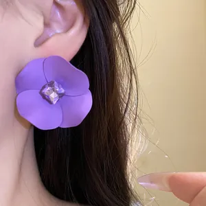 Primer plano de un pendiente de flor lila mate con centro de cristal en la modelo