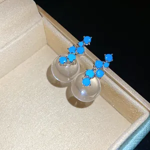 Close-up of minimalist silver needle earrings with blue zircon and clear resin ball charms