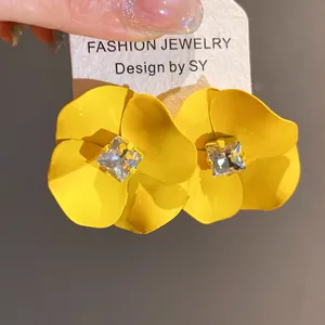 Primer plano de pendientes de flores amarillas lacadas con pedrería central