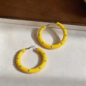 Primo piano di orecchini a cerchio in smalto giallo con pois blu e perni in argento massiccio.