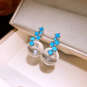 Close-up of minimalist silver needle earrings with blue stones and clear resin balls.