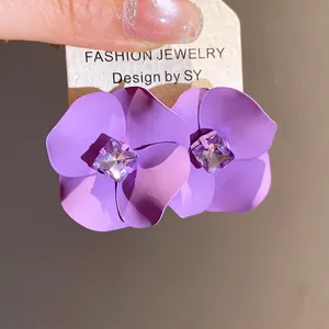 Primer plano detallado de pendientes de flores moradas mate con un cristal central.
