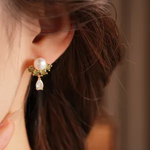 Dettaglio di orecchini placcati oro 18k con perla e pendente in zircone verde