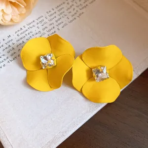 Primer plano de pendientes de flor amarilla con un diamante de imitación cuadrado central.