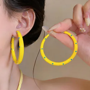 Primo piano di orecchini a cerchio in smalto giallo con pois blu su una modella femminile