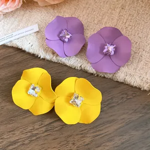 Primer plano detallado de pendientes de flores mate en púrpura y amarillo con cristales.