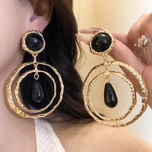Macro view of golden textured earrings with black resin teardrop pendant decoration