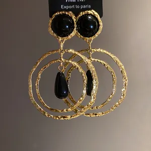 Detailed view of gold wrinkled metal hoop earrings with black resin teardrop