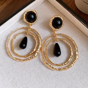 Detail view of luxury gold textured round earrings with black resin teardrop pendants