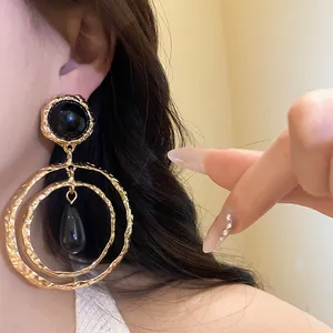 Close-up detail of gold-toned textured hoop earrings with black resin teardrop pendant.