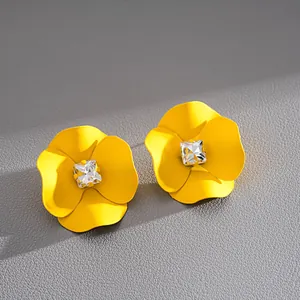 Detail view of yellow spray-painted flower stud earrings with square crystal centers