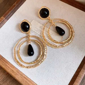 Close-up of vintage gold hammered metal earrings with black resin teardrop dangles.