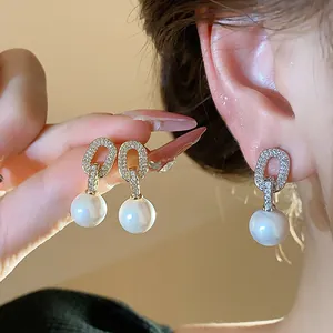 Detail of gold-plated zircon oval stud earrings with white pearls on ear