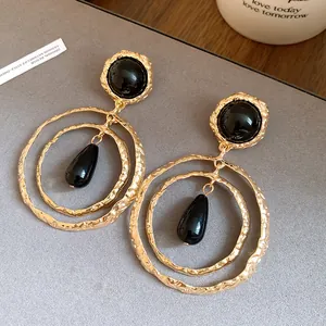 Close-up of vintage gold pleated earrings with black resin teardrop pendant detail